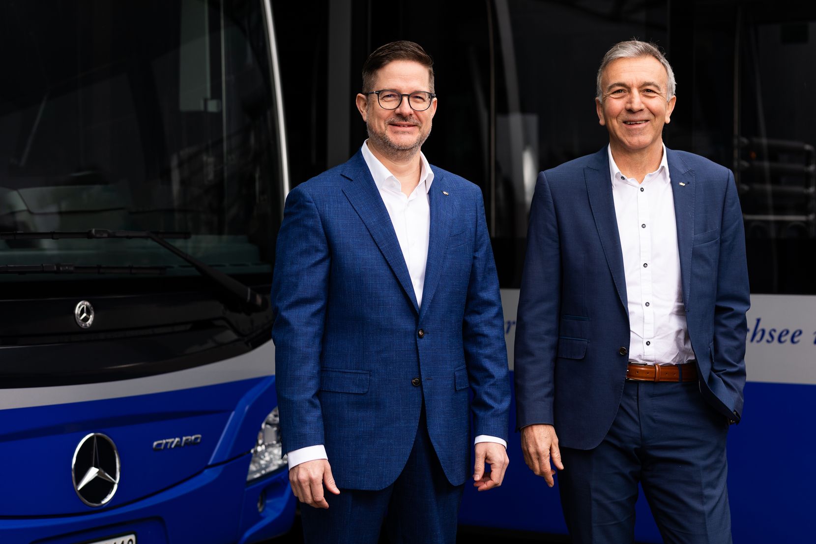 Der neue und der alte Direktor der VZO vor blauen Autobussen.