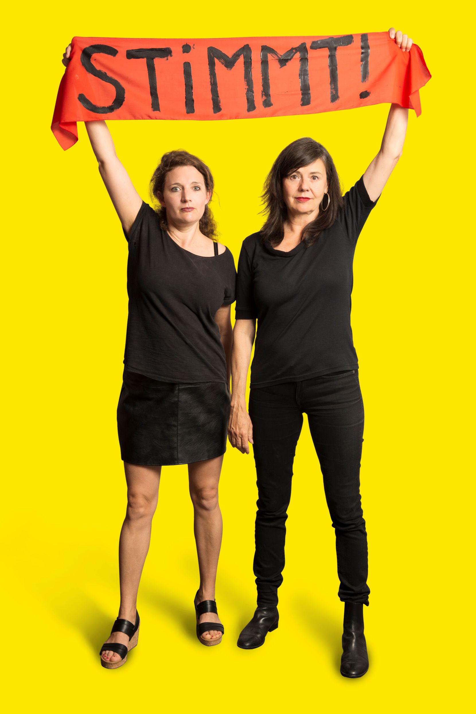 Zwei Frauen, ganz in Schwarz gekleidet, halten ein Banner in die Höhe, darauf steht «Stimmt!»