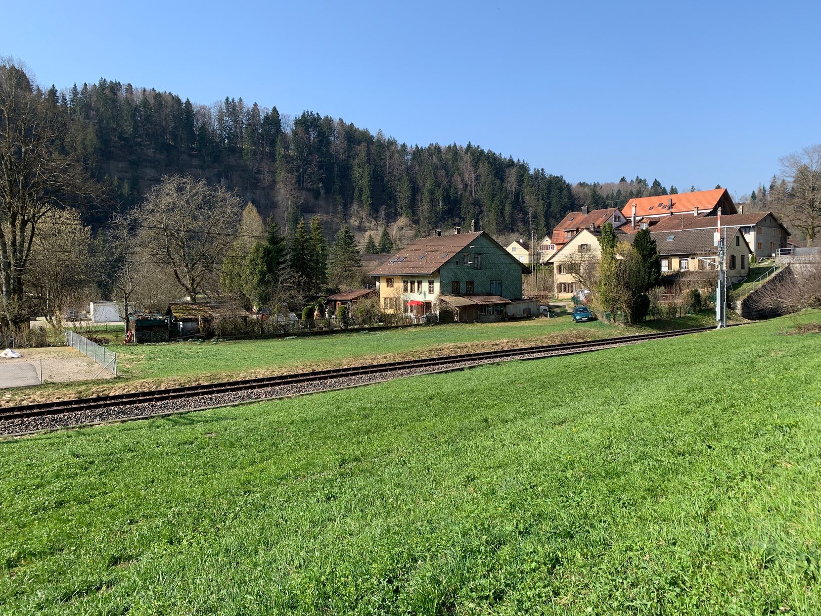 Eine Bahnlinie und dahinter eine Siedlung im Tösstal, dahinter Wald.
