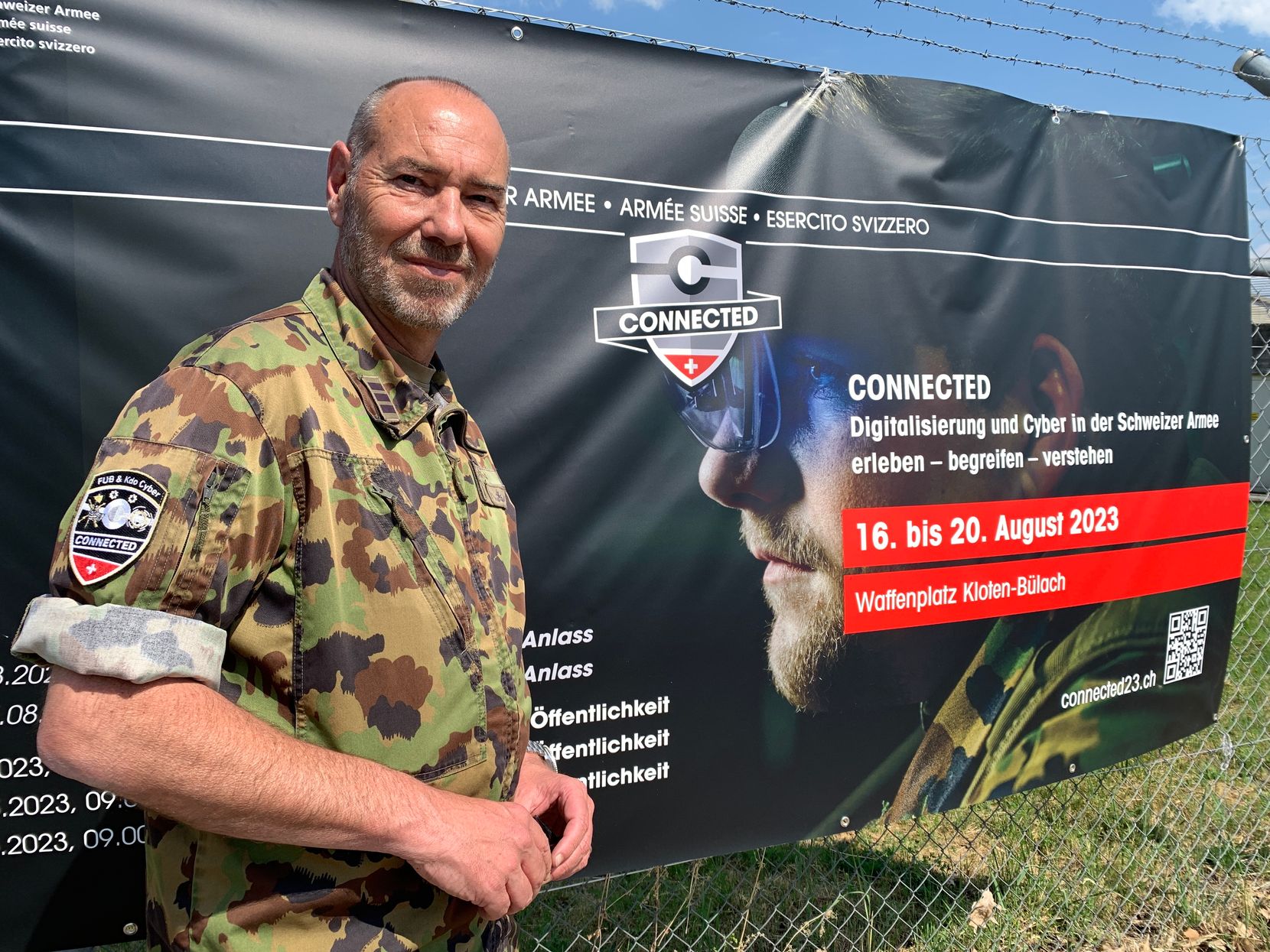 Berufsmilitär Oberst Pascal Martin vor einem Plakat des Grossanlasses Connected in Kloten.