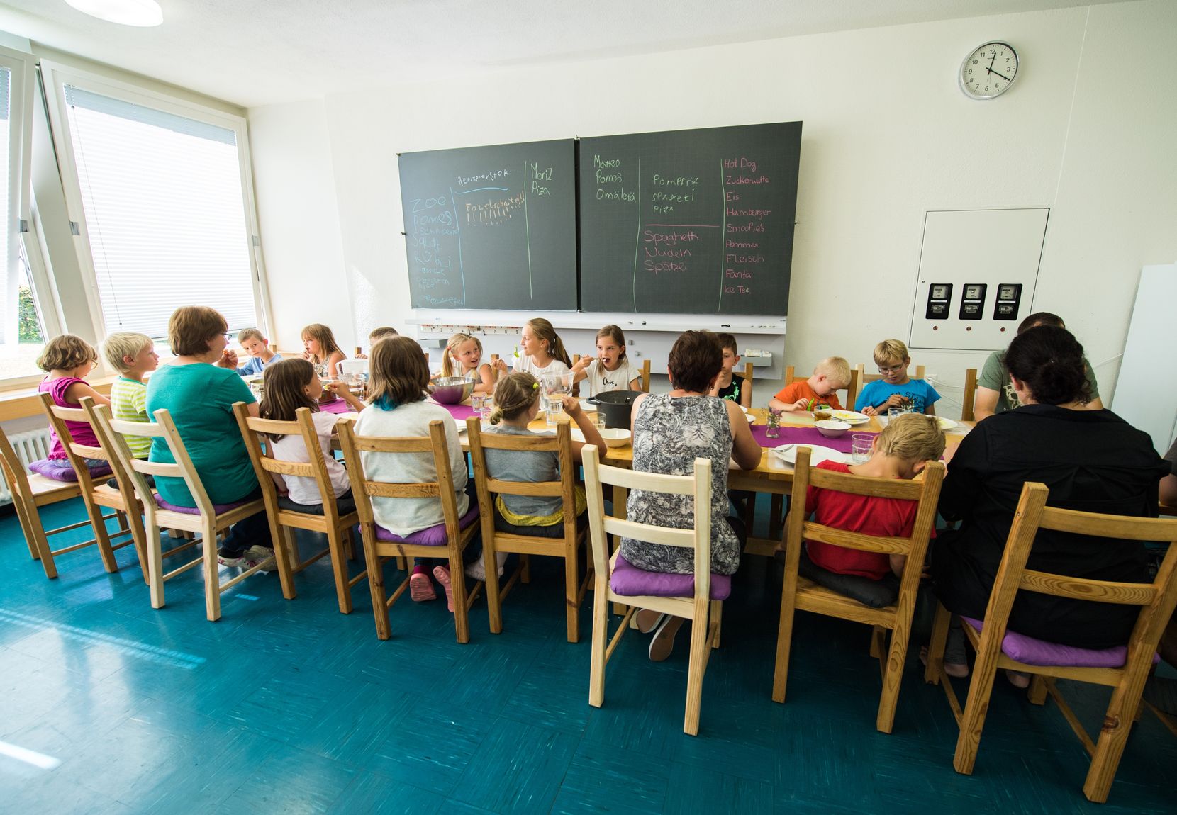 Kinder sitzen an einem Mittagstisch im Schulzimmer.