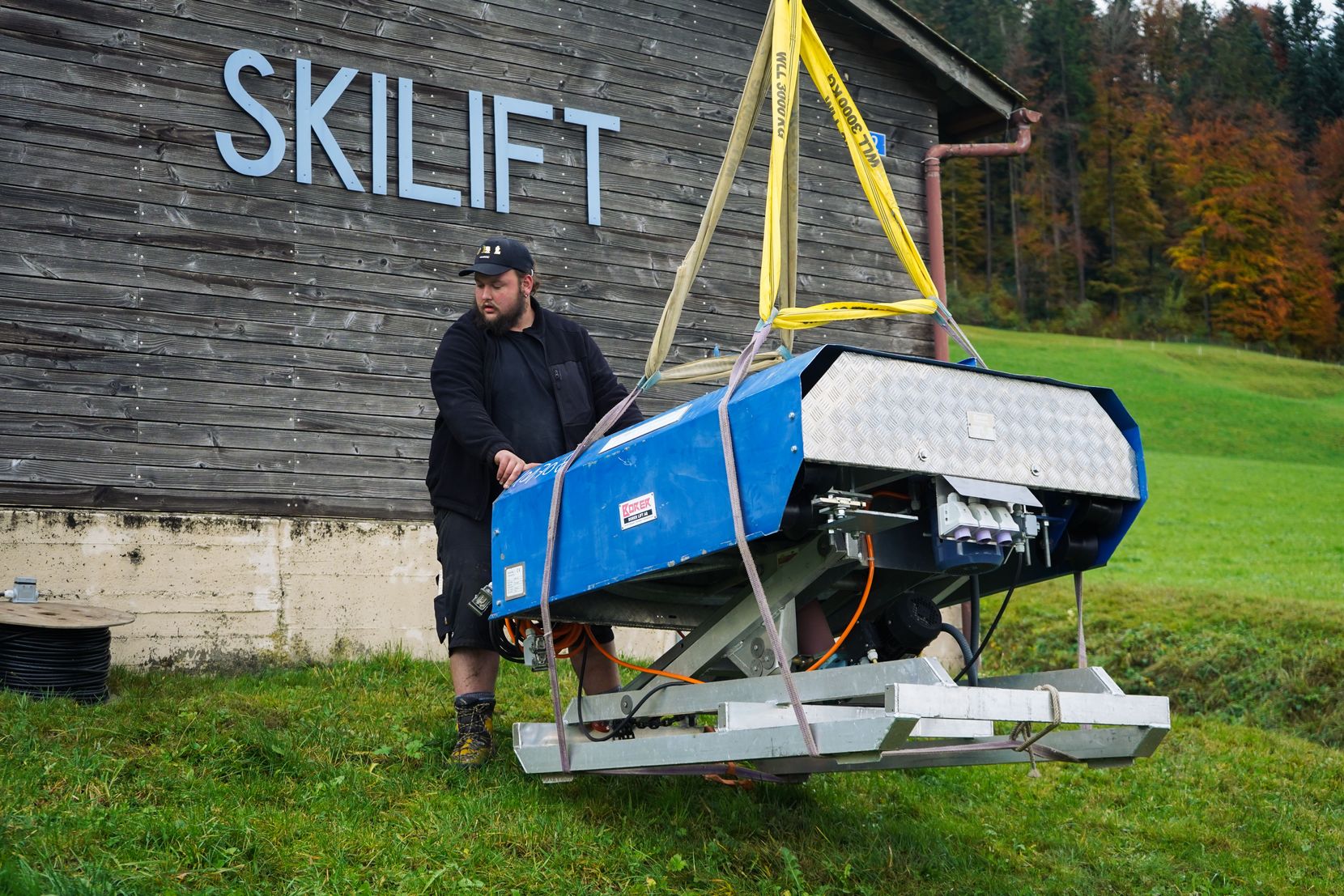 Ein Mann platziert eine Skiliftanlage, die an einem Kran hängt.