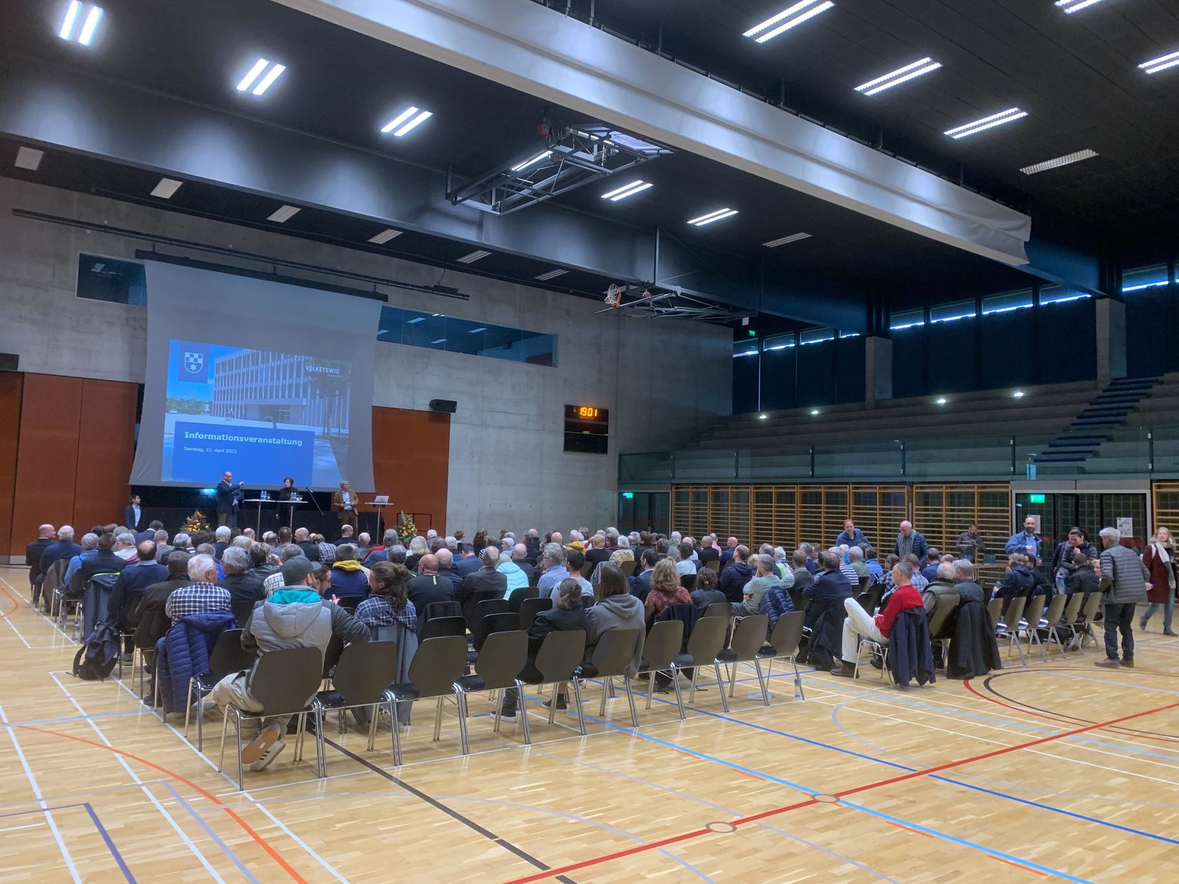 Viele Menschen auf Stühlen in einer Sporthalle.