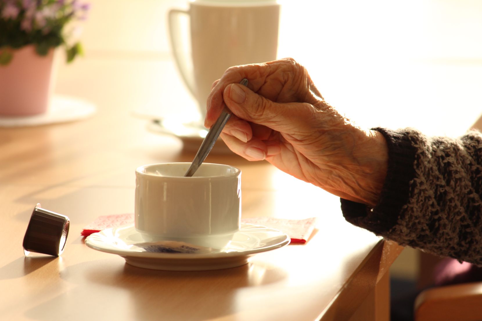 Das Foto zeigt die Hand einer alten Frau, die in ihrem Kaffee rührt. 