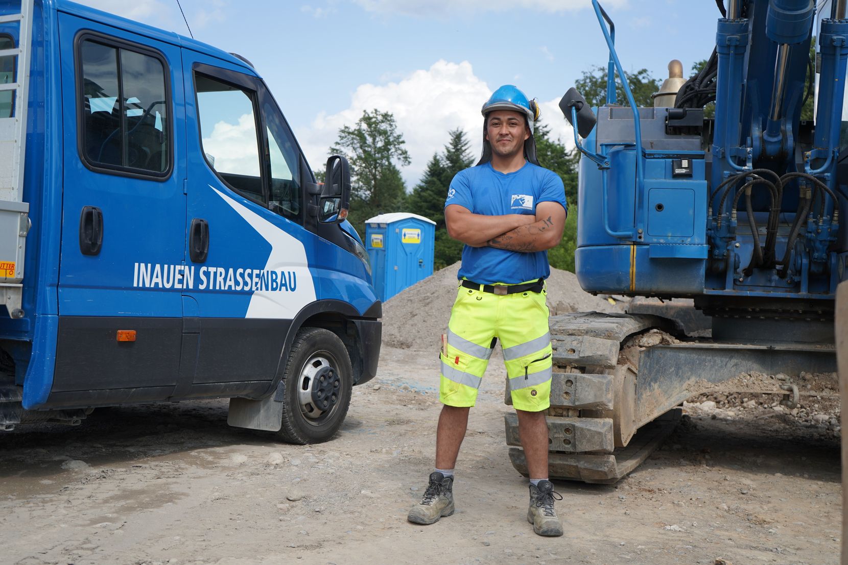 Ein junger Bauarbeiter in blauem Shirt und mit blauem Helm.