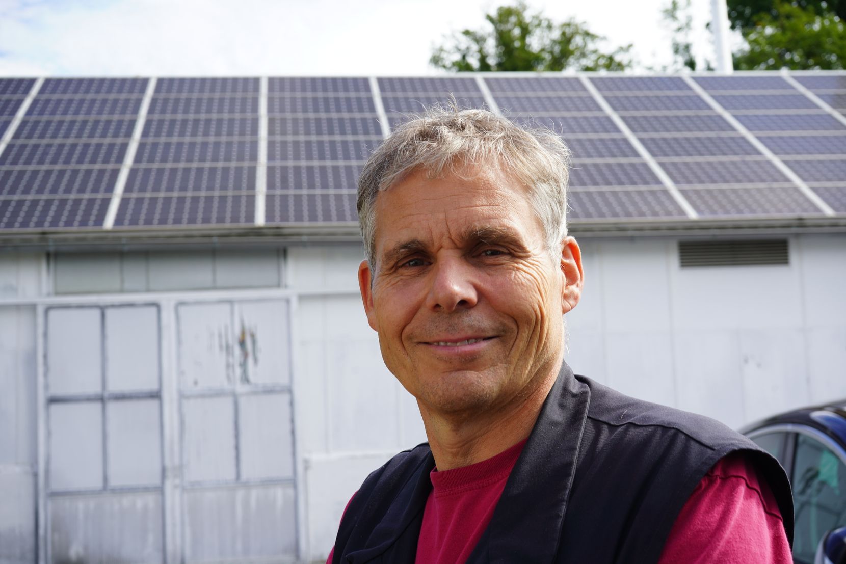 Ein Mann steht vor einer Halle, auf deren Dach Solarpanels installiert sind.