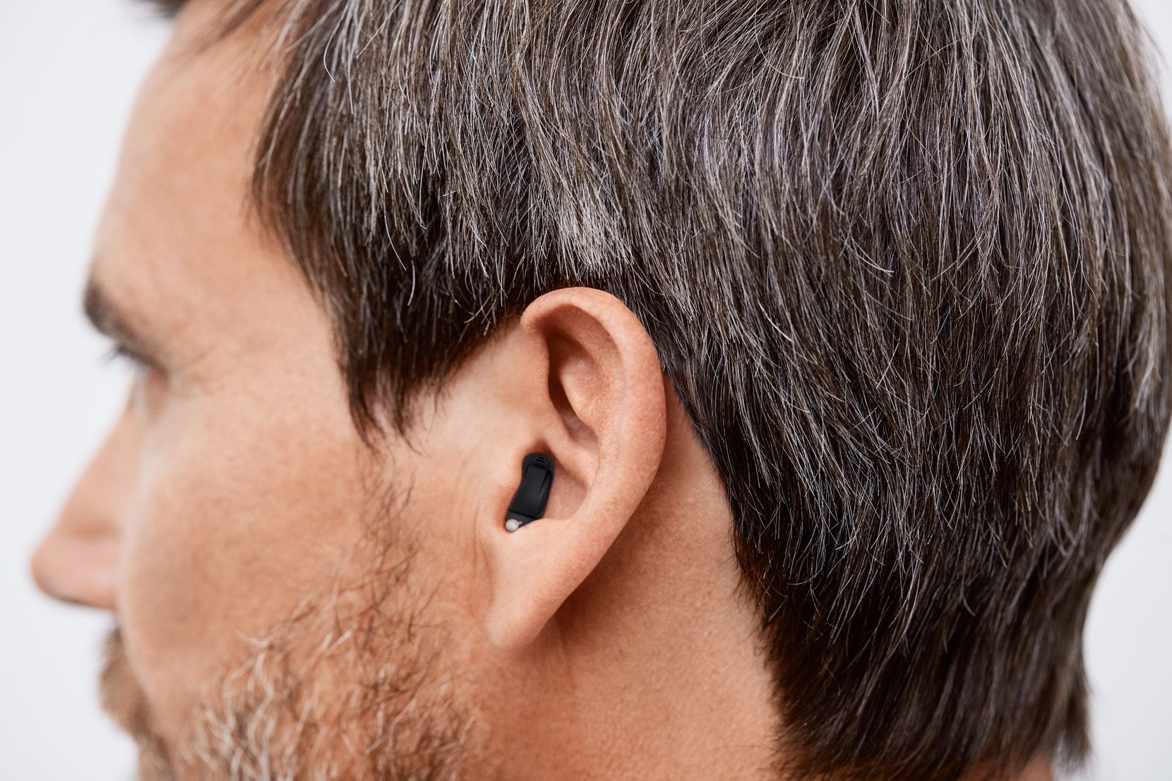 Der Kopf eines Mannes von der Seite aus fotografiert. Der Mann trägt ein kleines Hörgerät im Ohr.