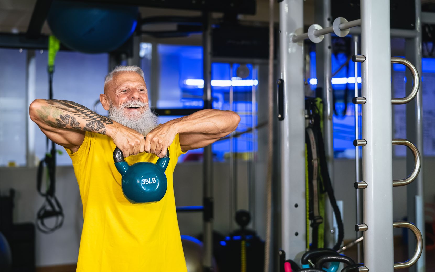 Man sieht ein älterer Herr, der in einem Gym Krafttraining macht und dabei sehr fröhlich aussieht. 