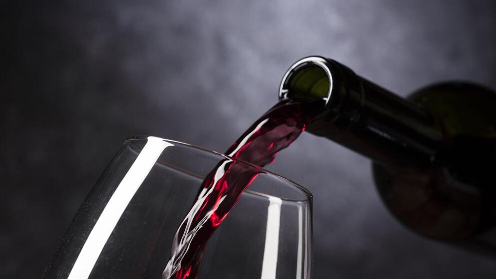 Aus einer Flasche wird Rotwein in ein Glas eingeschenkt.