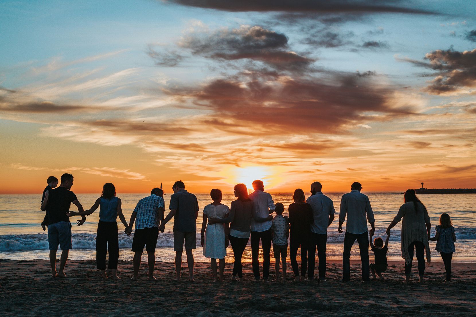 Auf dem Bild sieht man eine Gruppe von Menschen, die zusammen in einer Reihe stehen und den Sonnenuntergang am Meer geniessen.