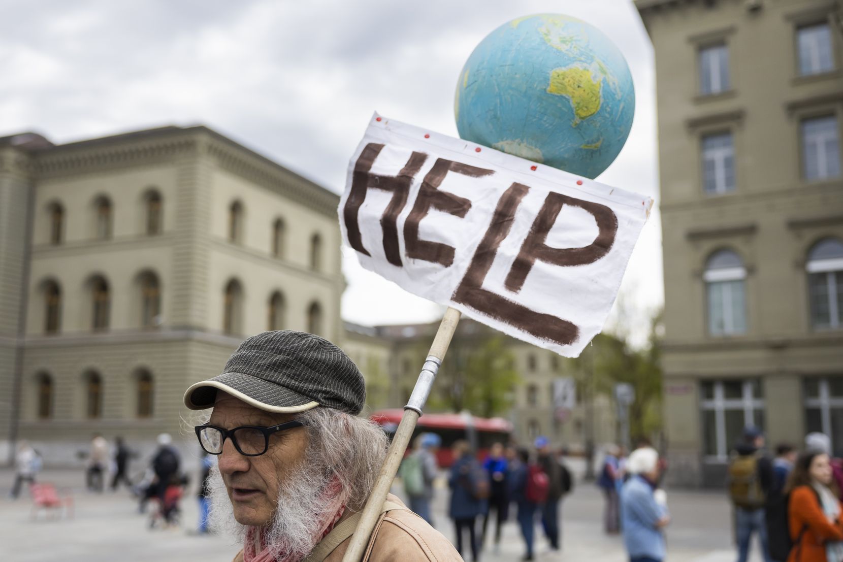 Ein Teilnehmer am La Marche Bleue haelt eine Weltkugel und ein Plakat mit der Aufschrift Help auf dem Bundesplatz.