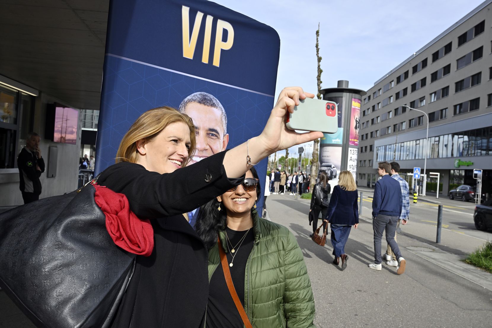 Zwei Frauen machen ein Selfie vor einem Plakat.
