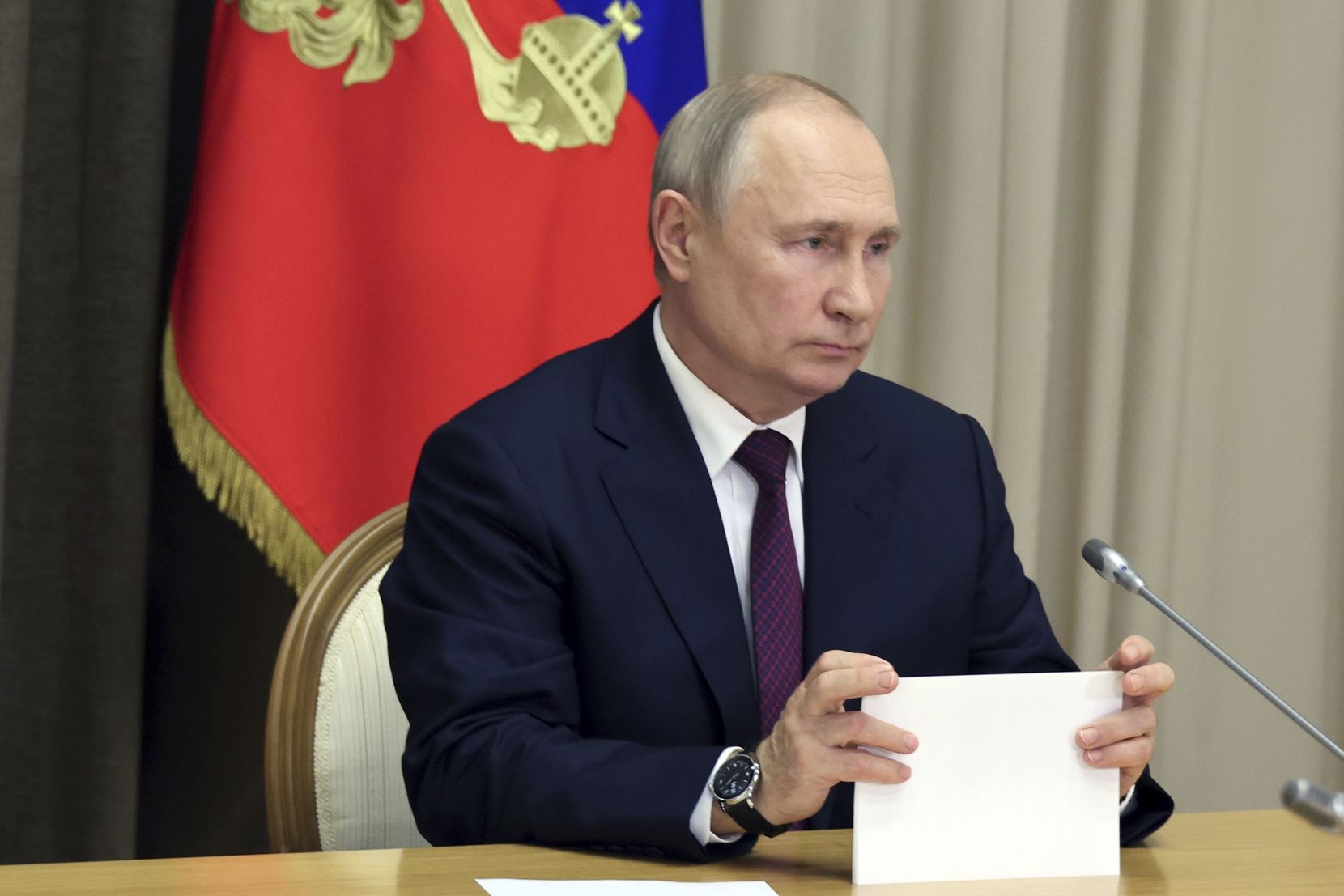 Wladimir Putin sitzt vor einem Mikrofon.