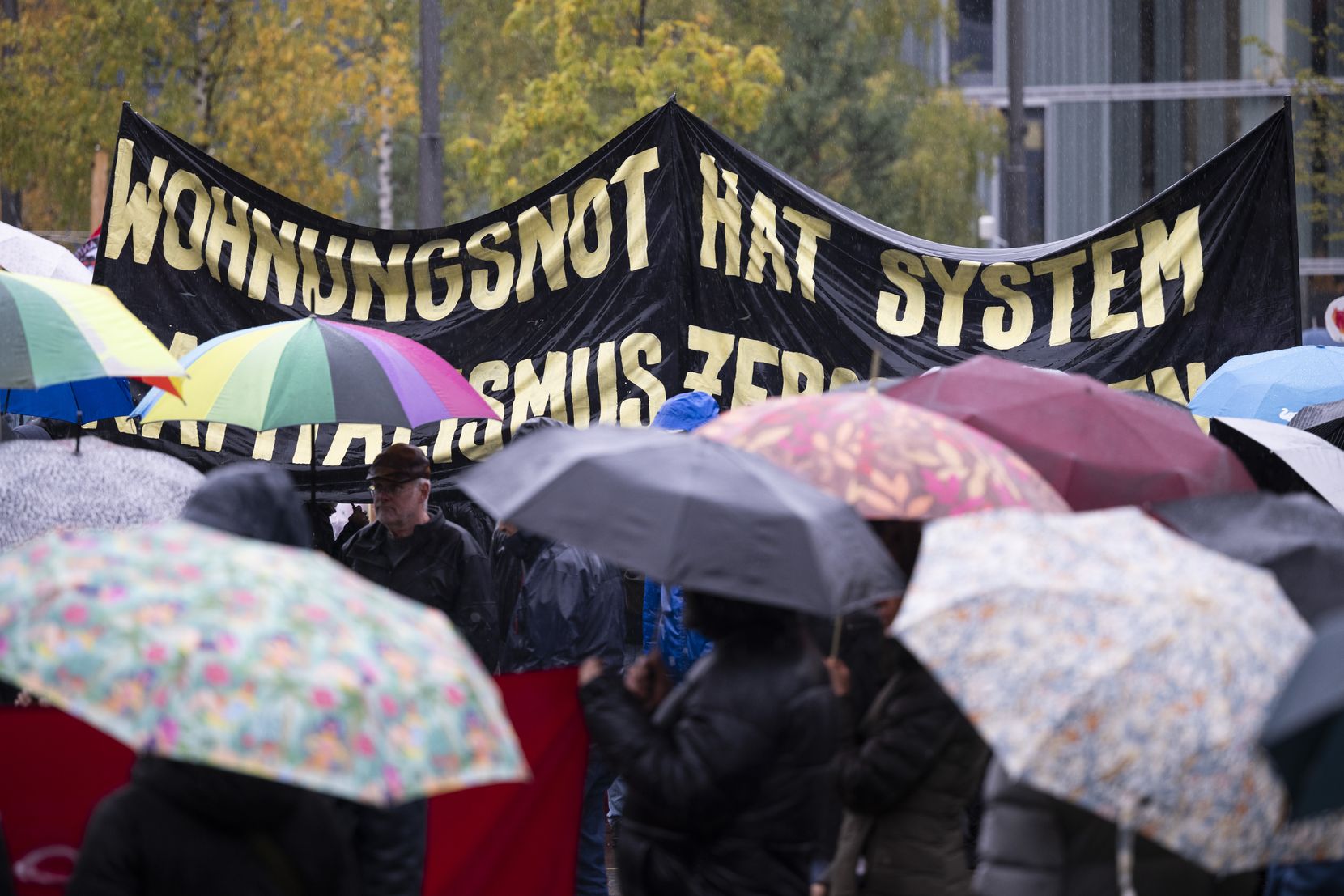 Demonstranten mit Schirmen und einem Plakat, auf dem steht: «Wohnungsnot hat System».