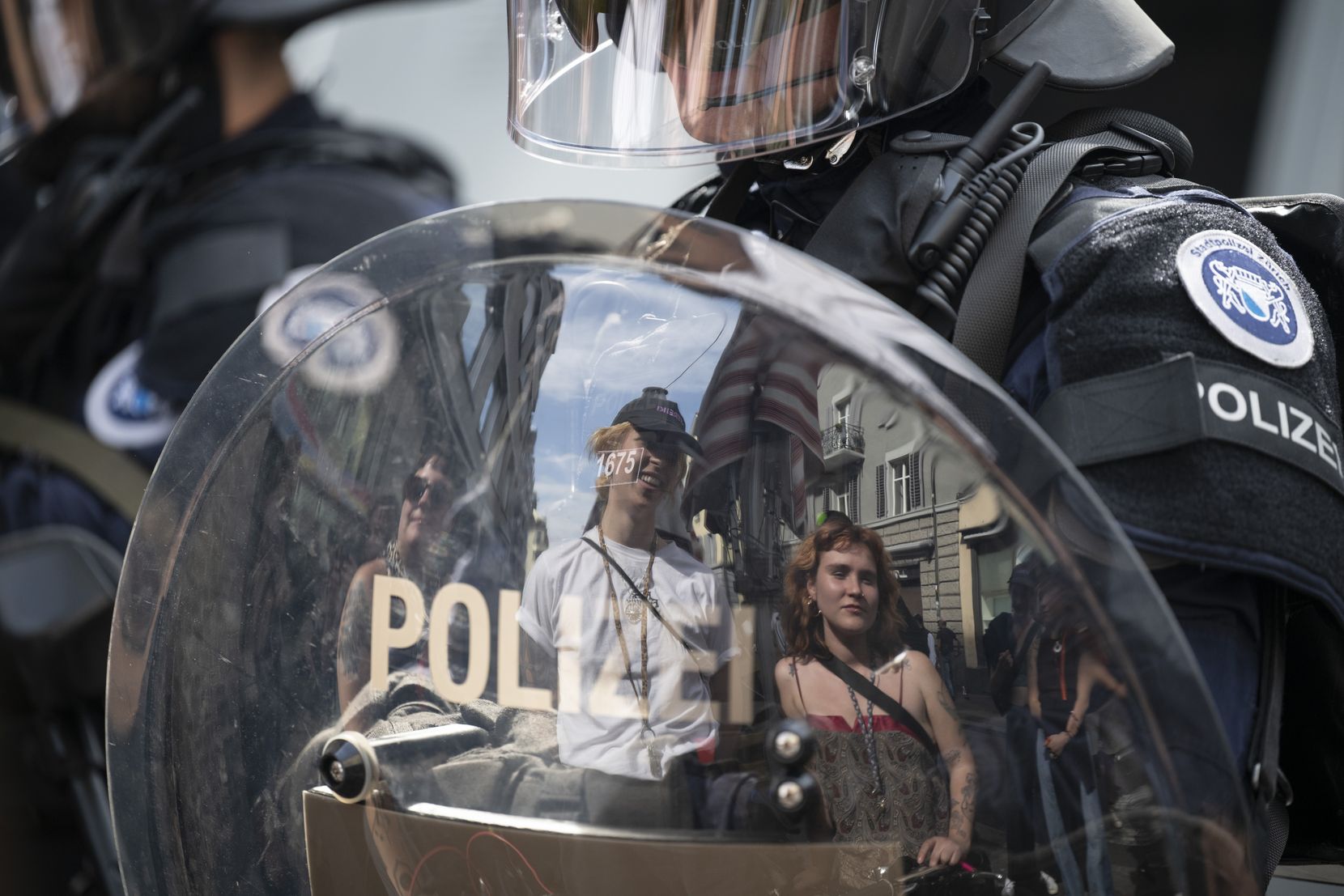 Man sieht das Spiegelbild von Demonstranten im Schild eines Polizisten.