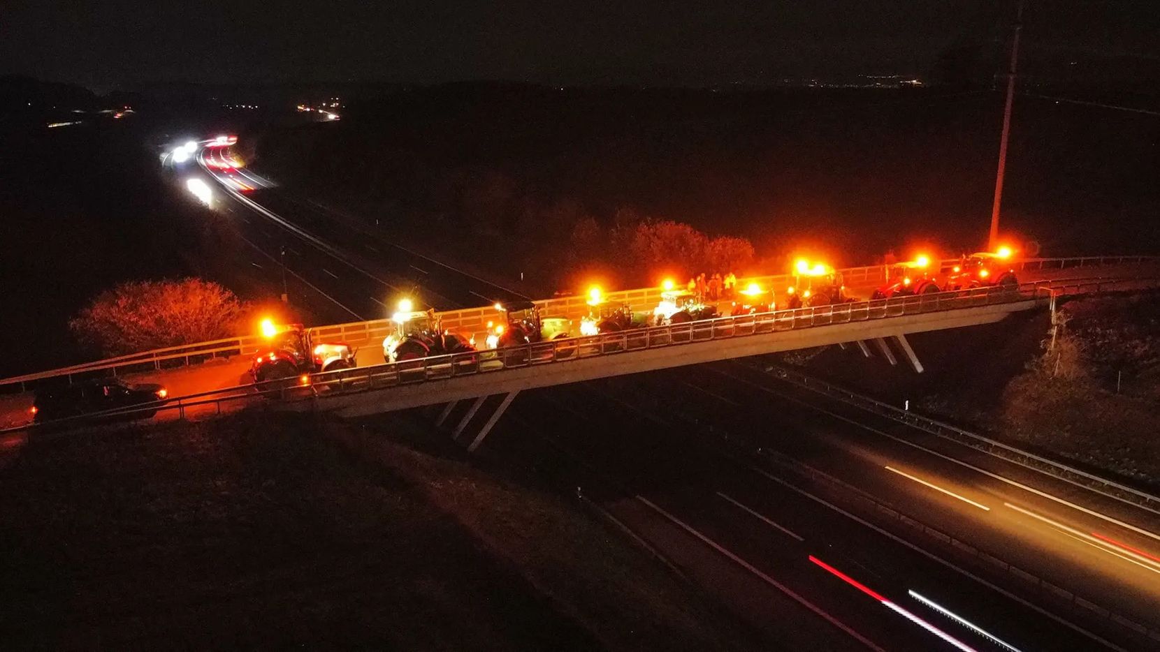 Traktoren mit Rundumleuchte auf einer Brücke im Dunkeln.