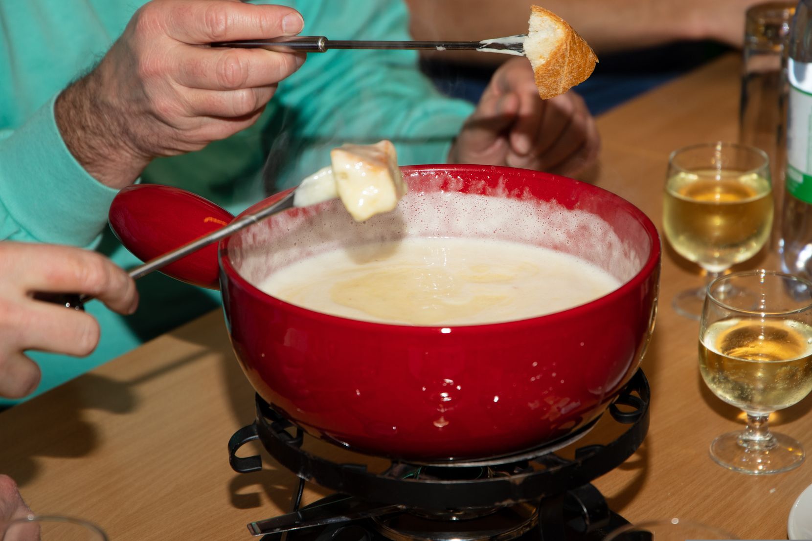 Man sieht ein Fondue-Caquelon und zwei Fondue-Gabeln mit in Käse getunktem Brot drauf.