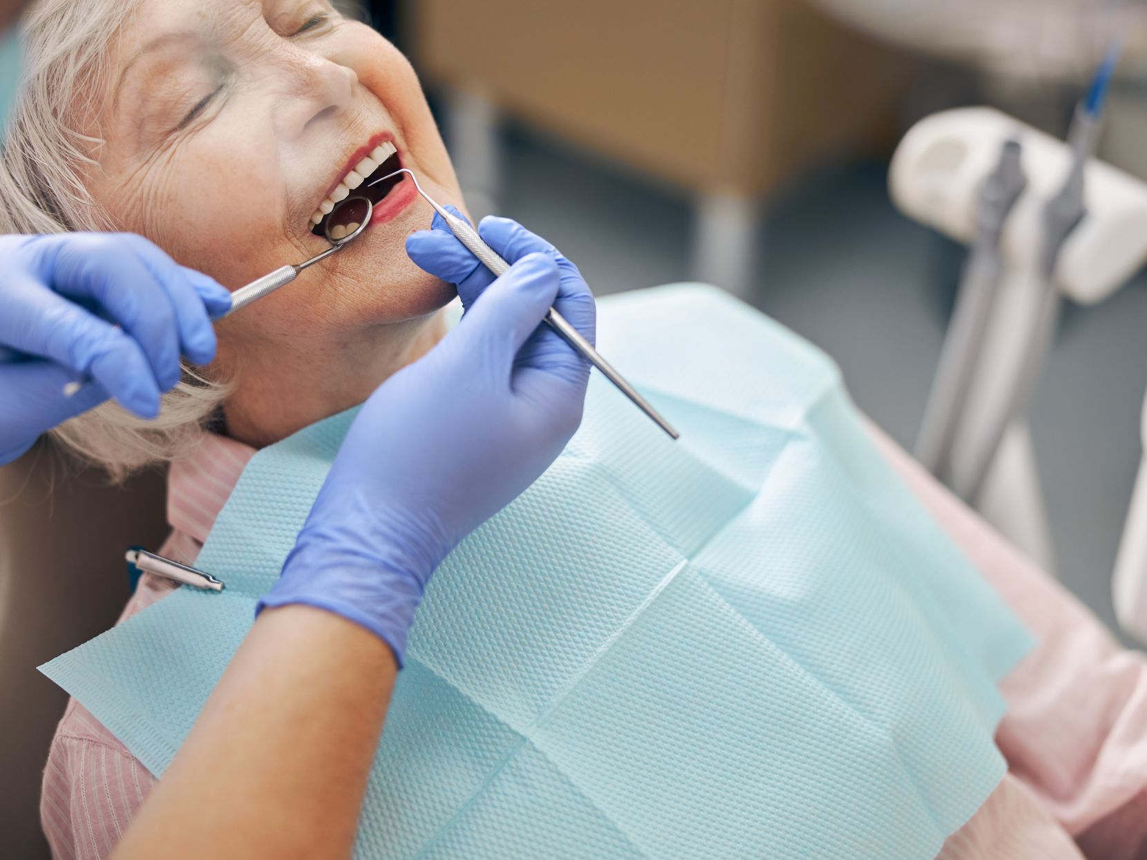Eine ältere Frau sitz auf einem Zahnarztstuhl und wird an den Zähnen behandelt.
