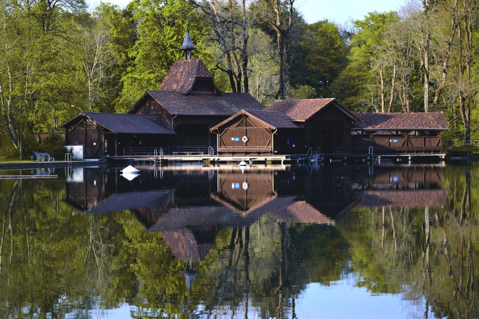 Ein Haus steht im Wald an einem spiegelglatten See.
