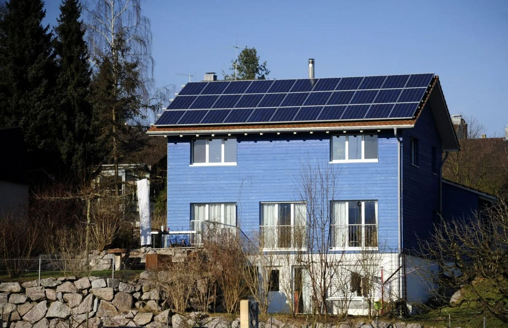 Ein Einfamilienhaus mit blauer Fassade und Solarpanels auf dem Dach.